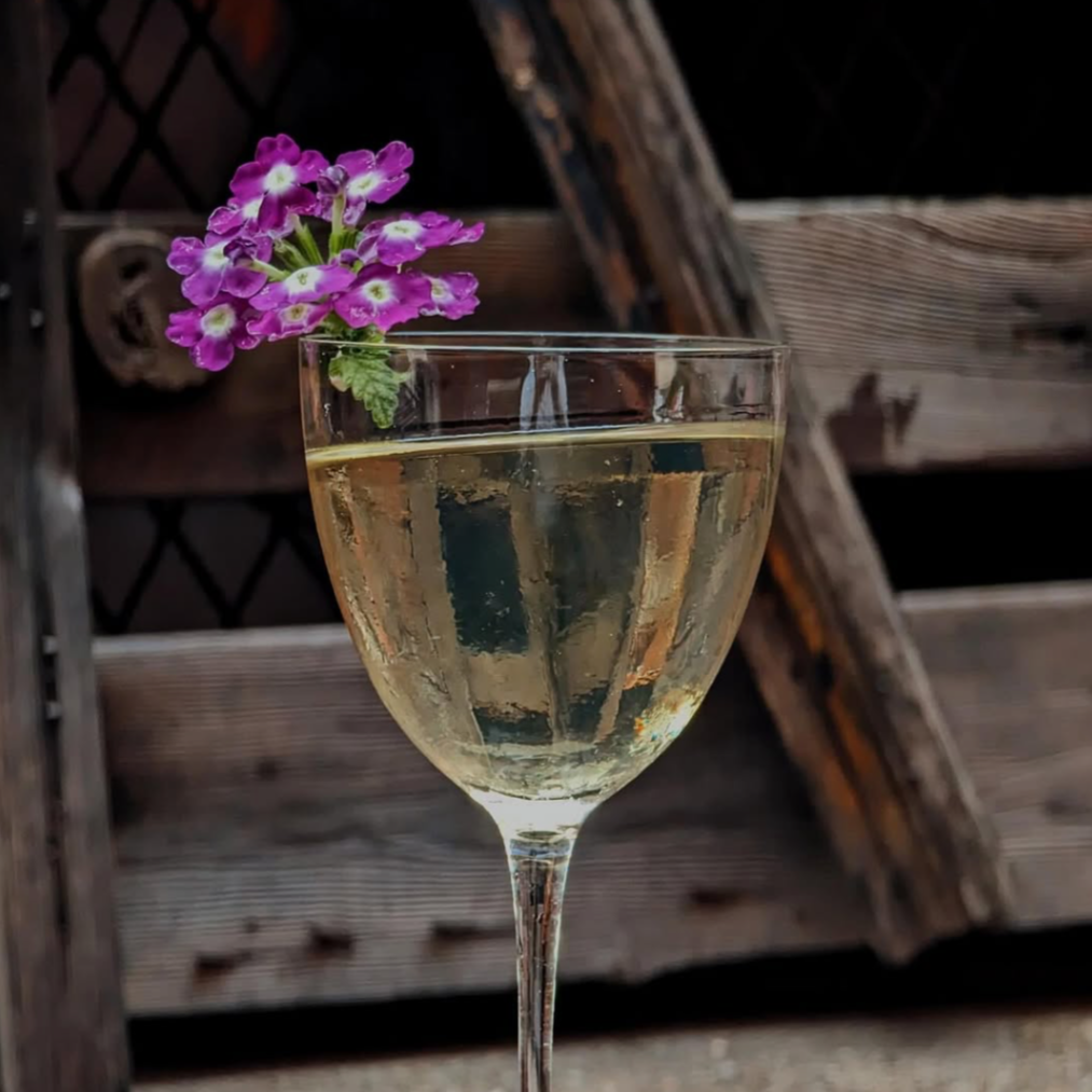 A glass of sparkling drink garnished with purple flowers, set against a wooden background.