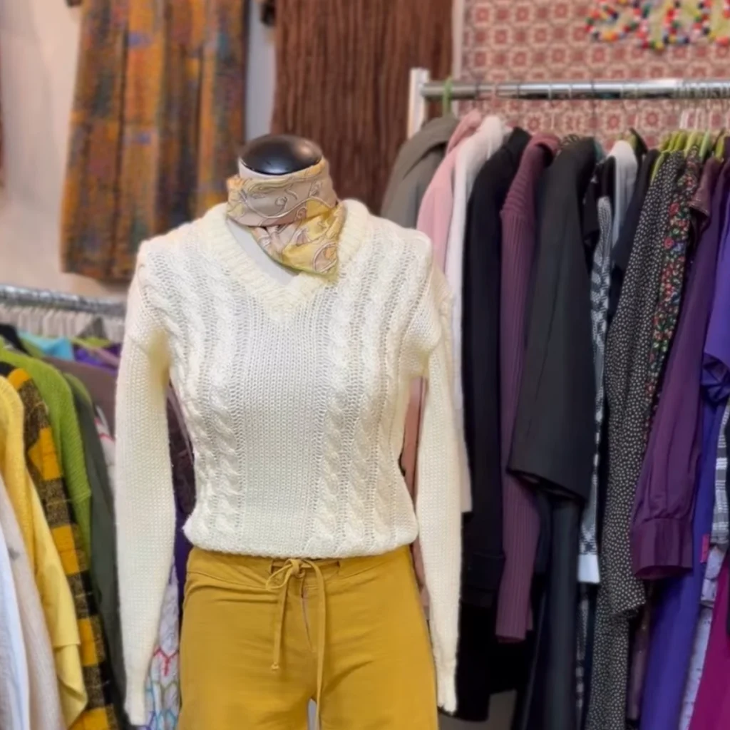 A cream cable-knit sweater and mustard pants displayed on a mannequin in a clothing store.