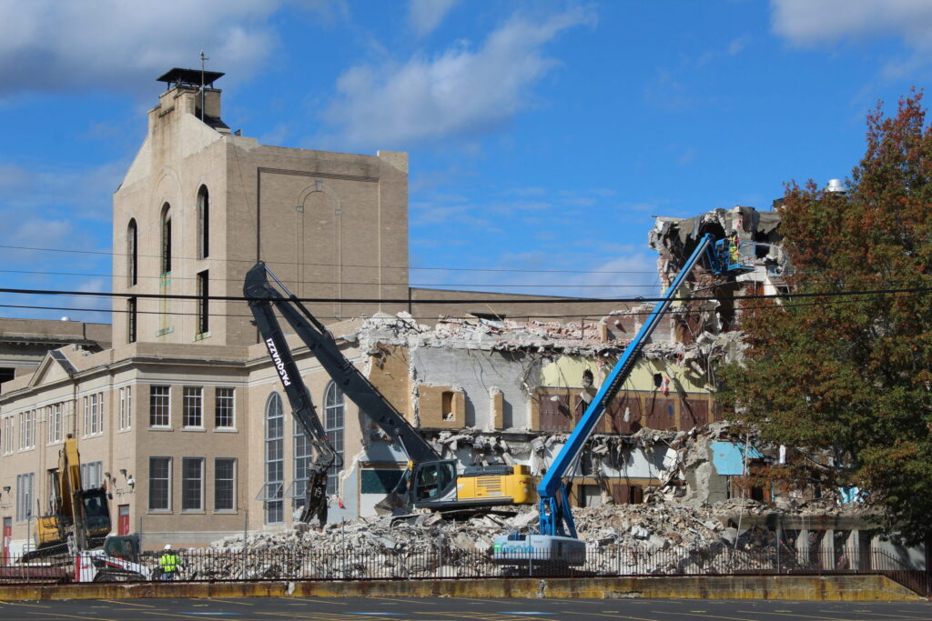 Demolition site with heavy machinery tearing down a building, blue sky above.