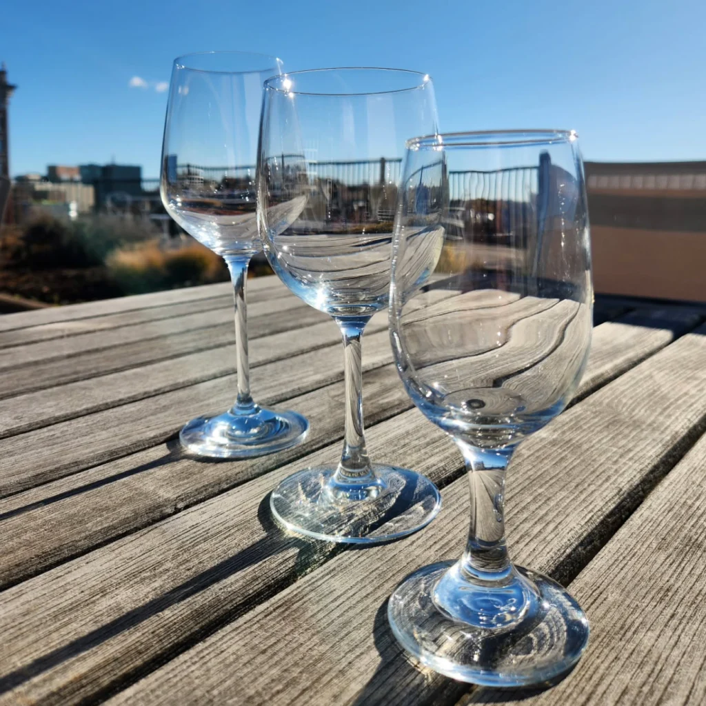 Three clear glass wine glasses on a wooden table, with a bright blue sky in the background.