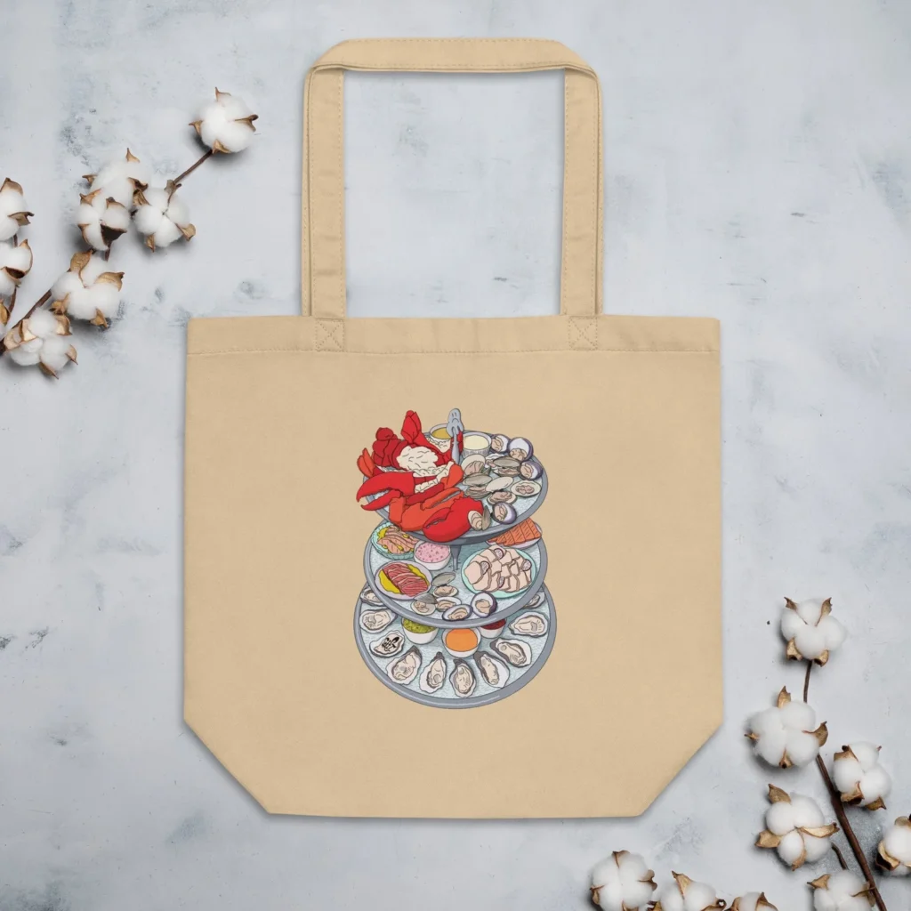 A beige tote bag features a colorful illustration of stacked seafood dishes, including a lobster and various shellfish.
