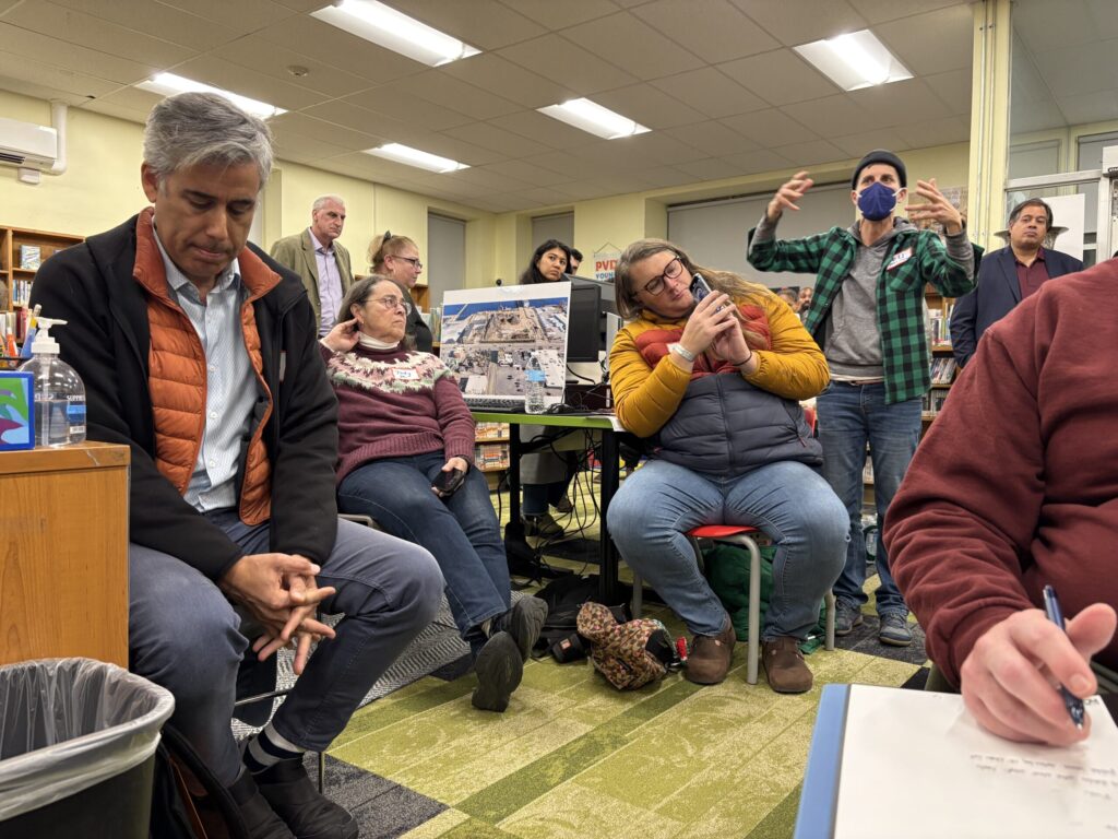 A group of people engaged in discussion in a library, with one person gesturing and others listening.
