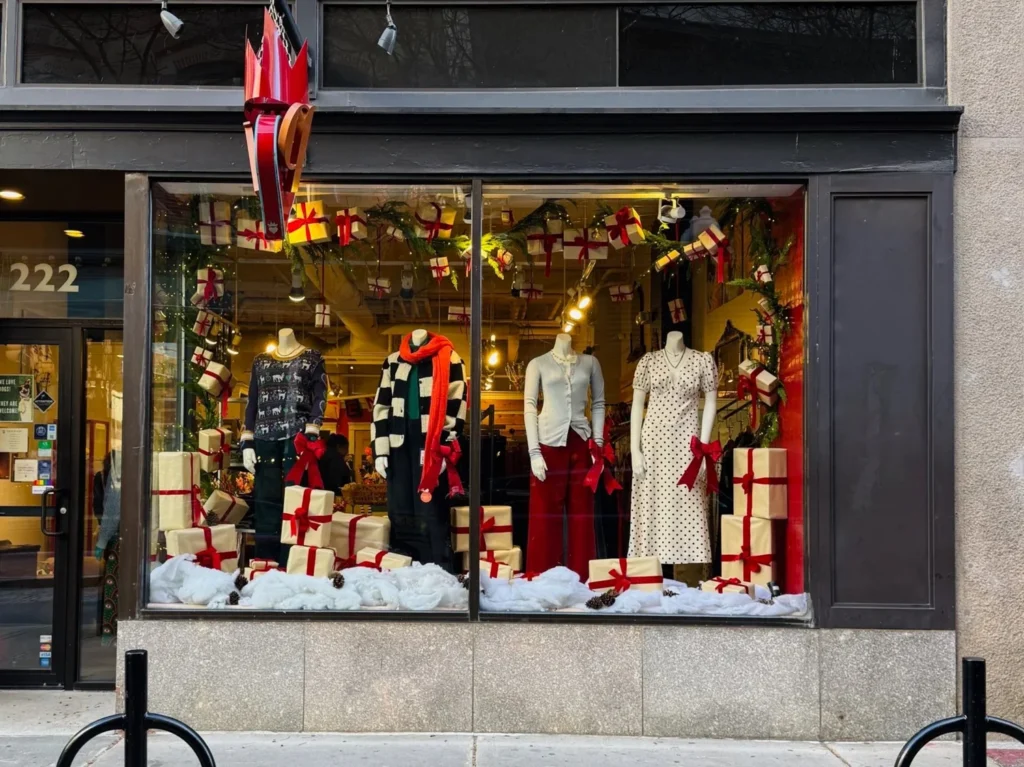 Storefront display features mannequins in festive clothing surrounded by wrapped gifts and holiday decorations.