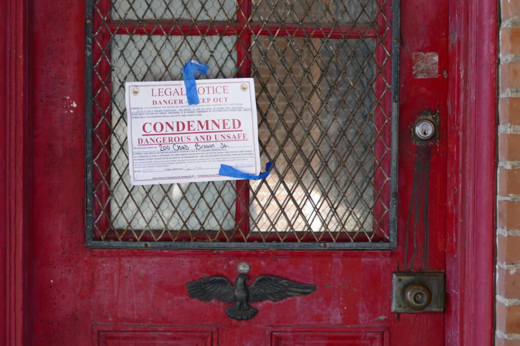 A red door with a legal notice labeled "Condemned" attached, warning it is dangerous and unsafe.