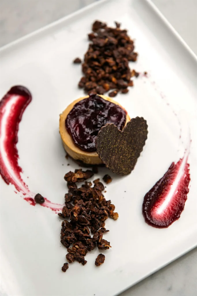 A dessert plate featuring a cheesecake topped with berry jam, chocolate heart, and granola clusters.