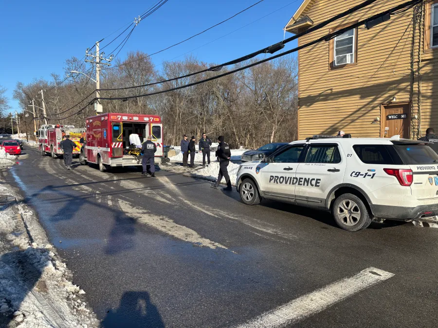 Emergency responders gather near fire trucks and a police vehicle on a snowy street.