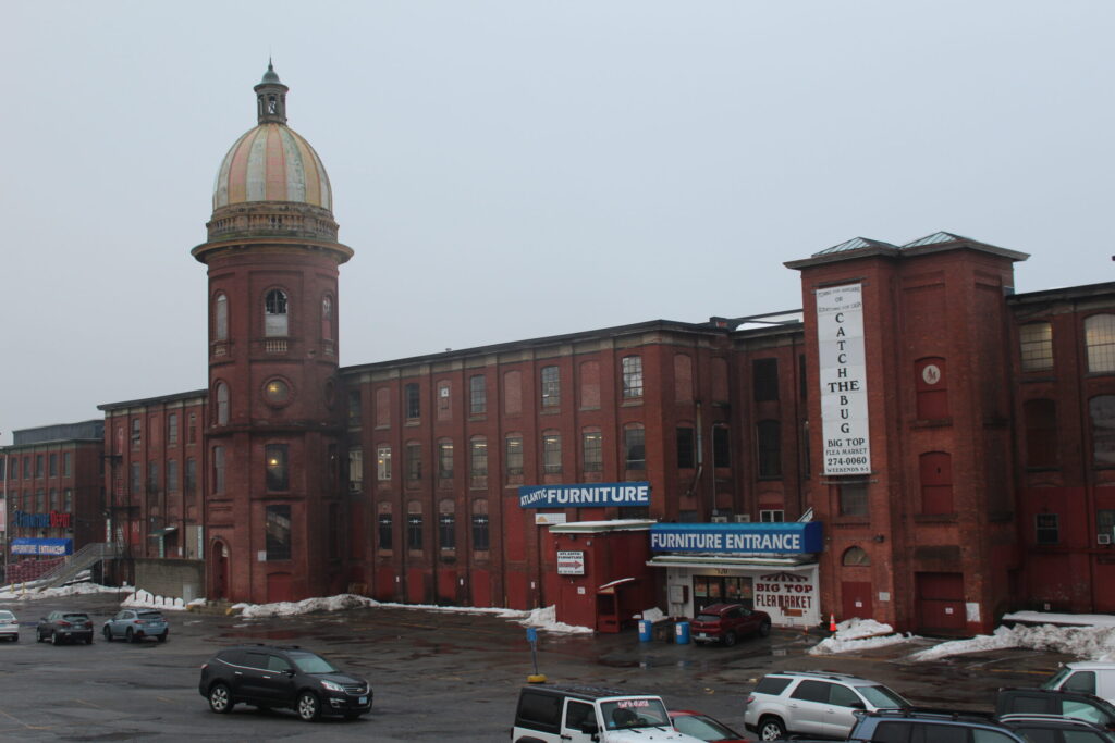 Red brick building with a dome, featuring signs for furniture and a flea market. Snow on the ground.