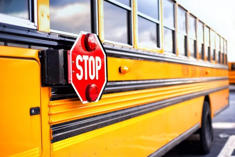 A yellow school bus displays a red "STOP" sign with lights activated.