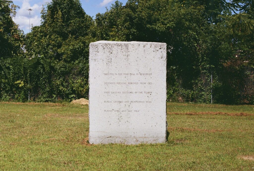 A stone monument with engraved text commemorating deceased persons reinterred in 1964.