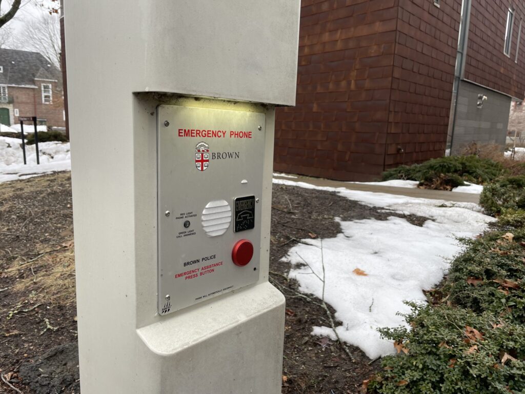 Emergency phone mounted on a post, with snow and shrubs in the background.