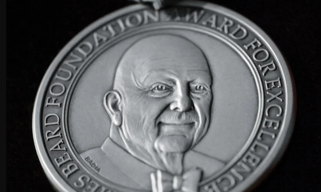 Silver medal featuring a smiling man's portrait, inscribed with "James Beard Foundation Award for Excellence.