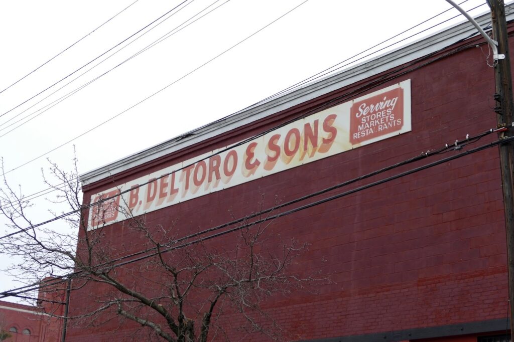 Sign on a red brick building reads "B. Deltoro & Sons," advertising services for stores and restaurants.