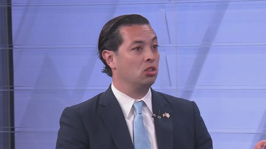 A man in a suit speaks during a discussion, gesturing with his hands.