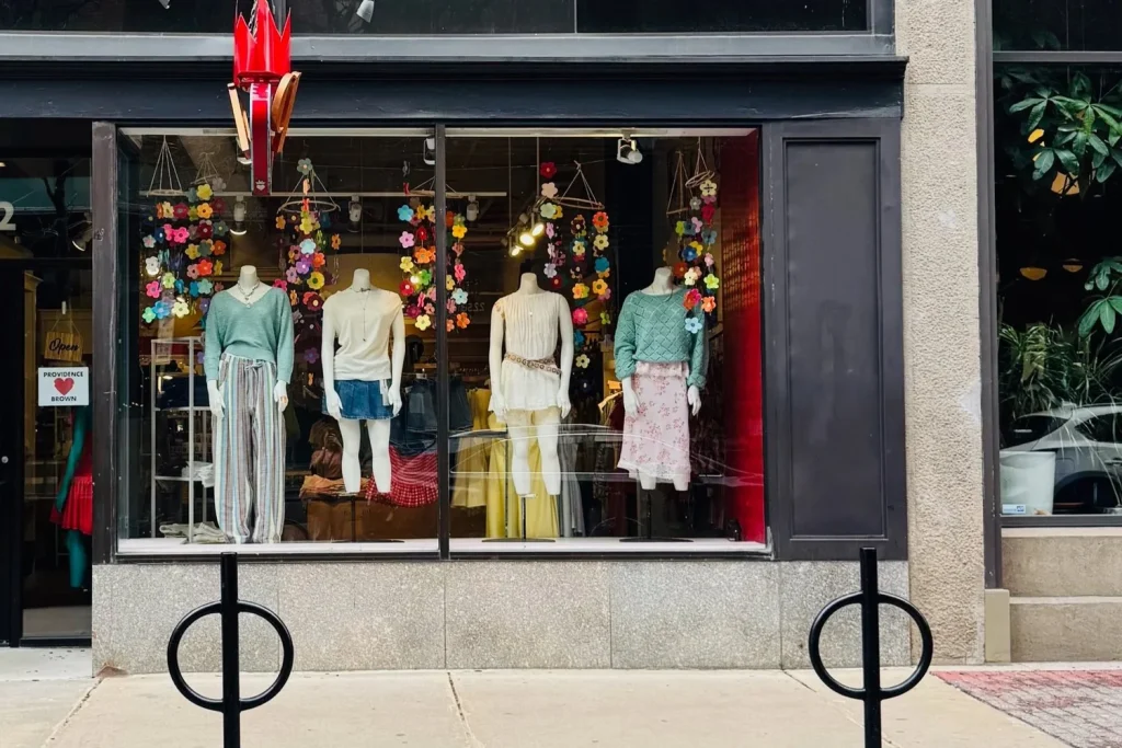 Storefront displays four mannequins in colorful outfits, surrounded by flower decorations.