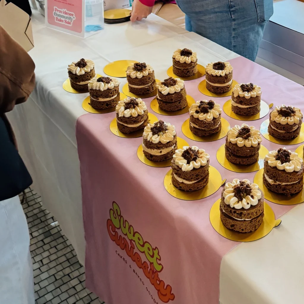 A table displays multiple small layered cakes with frosting and decorative toppings.