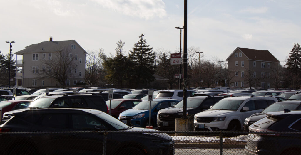 A crowded parking lot with various vehicles and two multi-story buildings in the background.