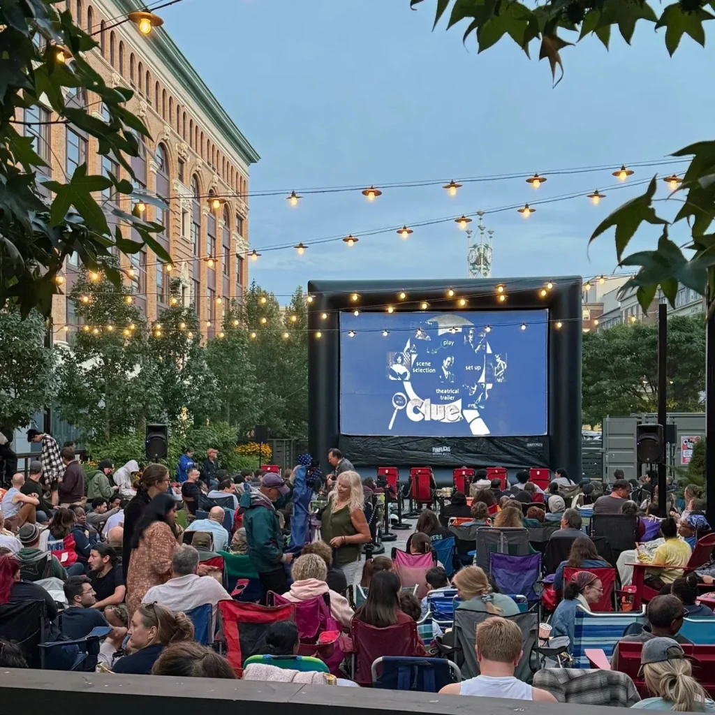 Outdoor movie screening with a large inflatable screen and a crowd seated on chairs.