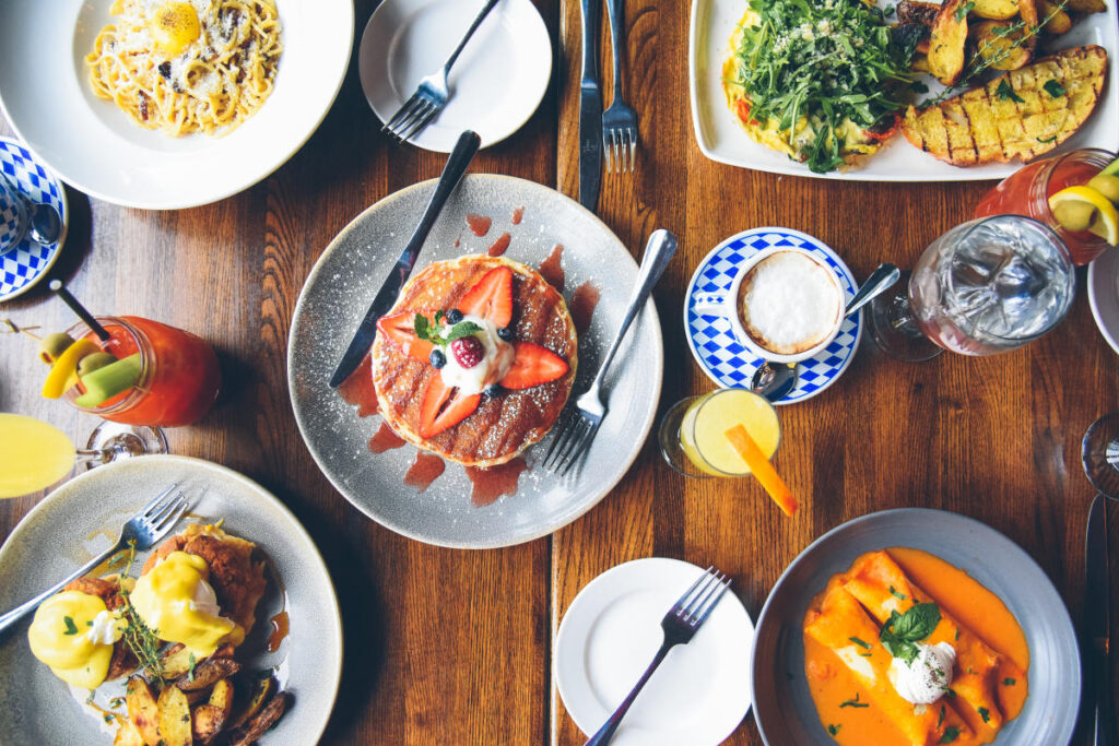 Aerial view of a table with various dishes, including pancakes, eggs Benedict, and drinks.
