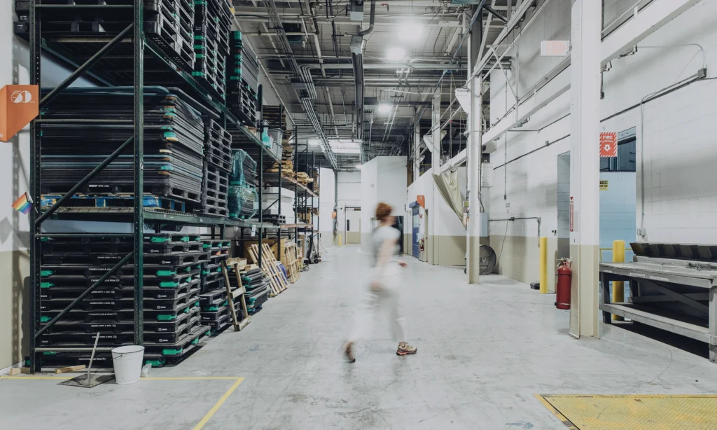 A person walks through a spacious warehouse with stacked pallets and storage areas.