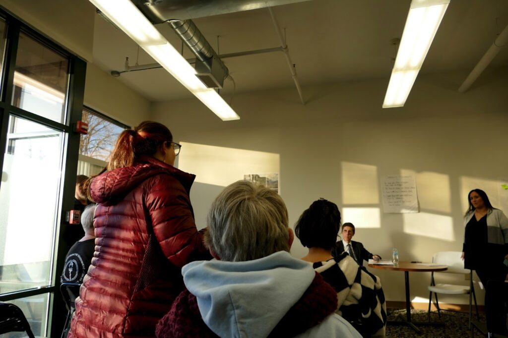 A woman stands and speaks to a group seated in a meeting room. Two people listen attentively.
