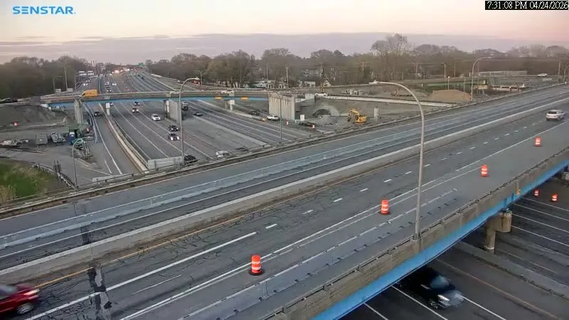 Traffic flows on a highway with construction barriers and visible roadwork in the background.