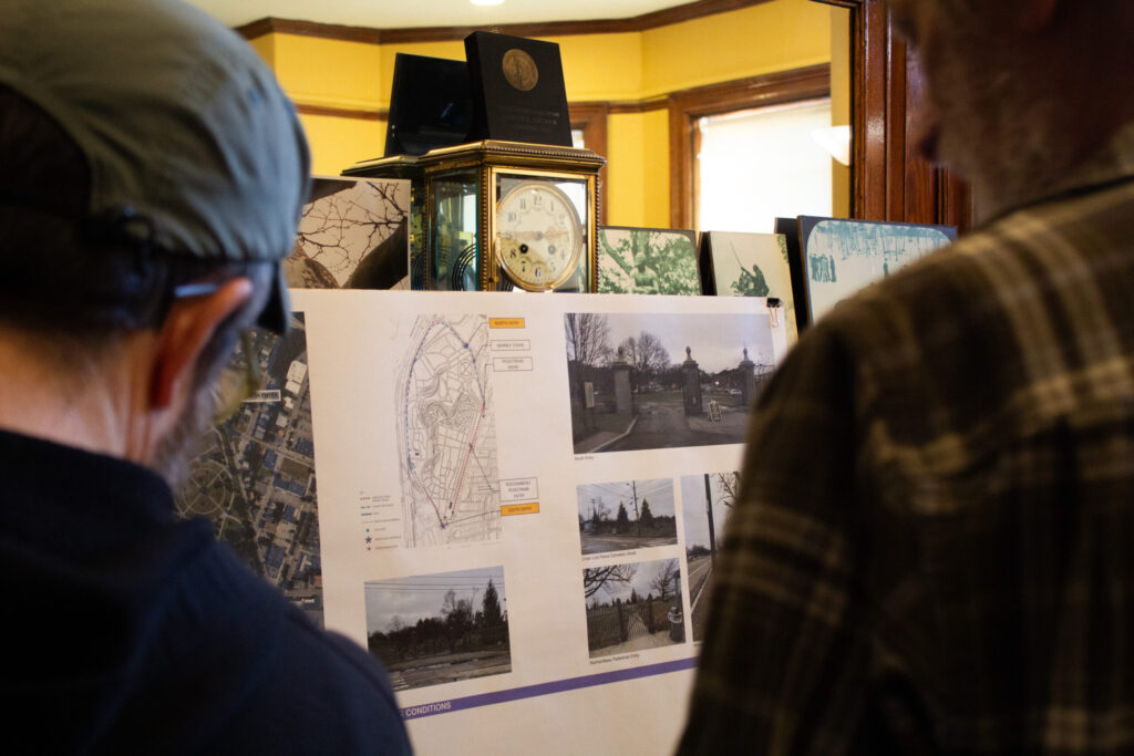 Two people examine a display board featuring maps and photographs of a park or cemetery.