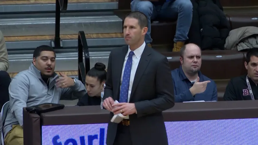 A coach stands near the bench while spectators engage in conversation.