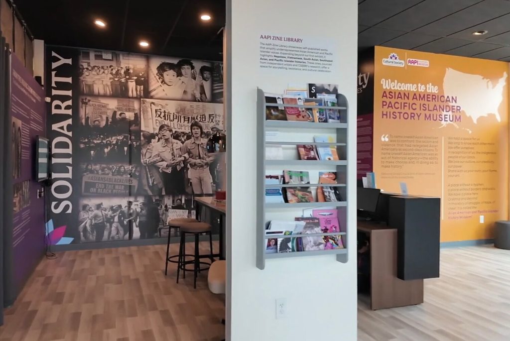 Interior of the Asian American Pacific Islander History Museum featuring a zine library and solidarity-themed wall art.