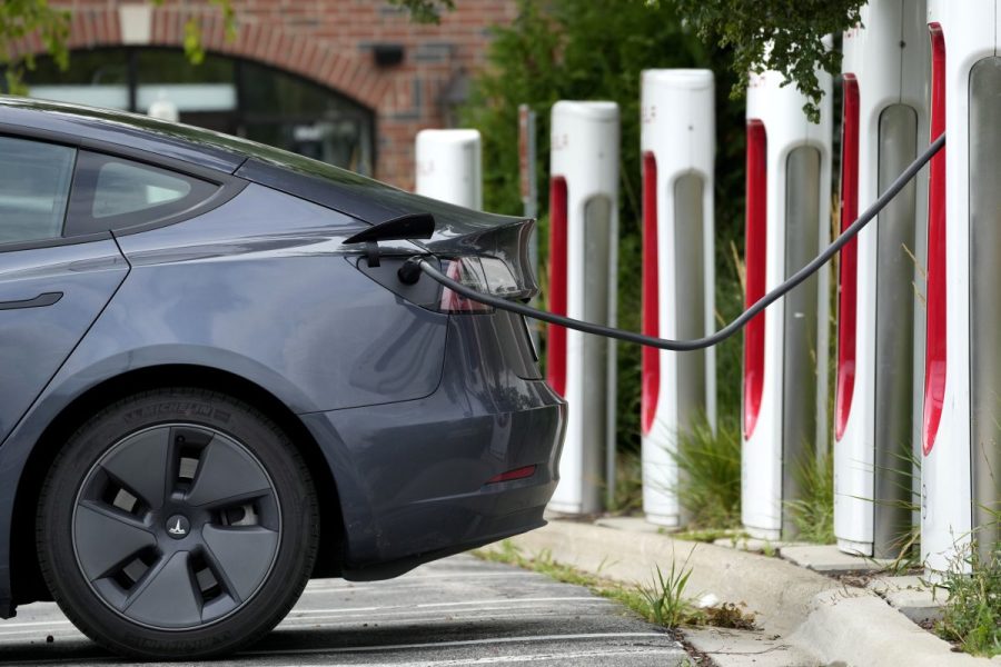 A gray electric car is charging at a station with multiple charging posts.