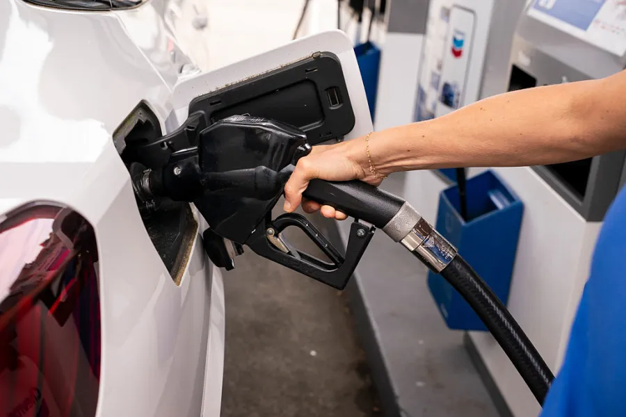 A person holds a fuel pump nozzle, refueling a white car at a gas station.