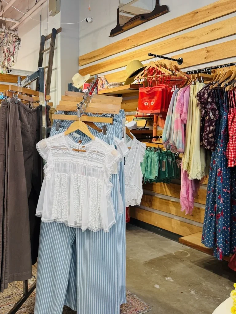 A white lace top hangs over blue striped pants in a clothing store with various garments displayed.