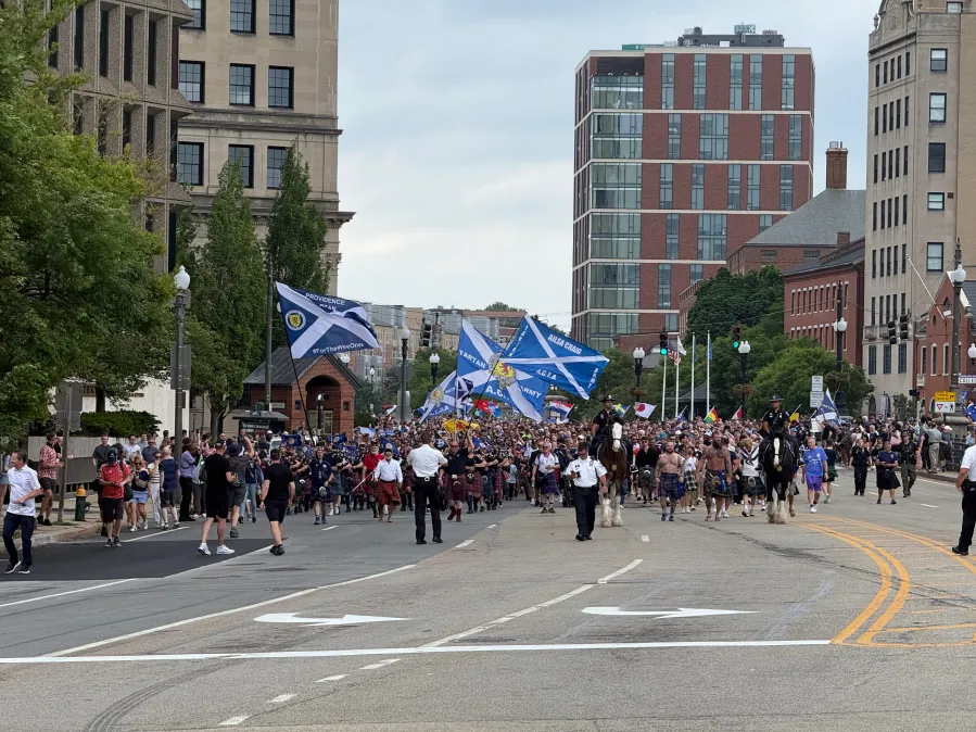 A large crowd marches down the street, carrying flags and accompanied by police on horseback.
