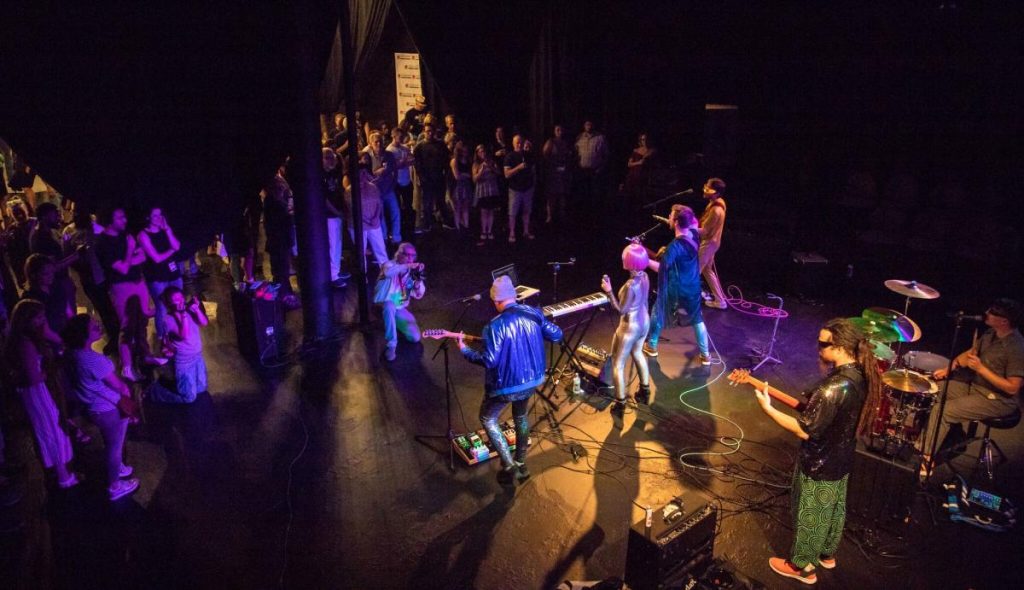 A lively band performs on stage while an audience enjoys the show, capturing the energetic atmosphere.