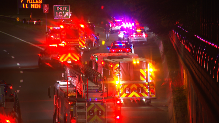Emergency vehicles with flashing lights respond on a highway, with traffic signs indicating distance and exit.