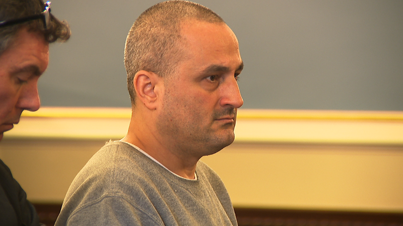 Two men sit in a courtroom; one looks serious while the other appears focused on him.