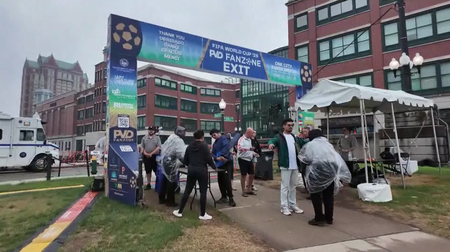 Crowd exits FIFA World Cup 2026 fan zone under a banner, with tents and buildings in the background.