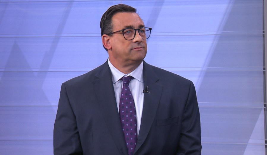 A man in a suit and glasses looks thoughtfully to the side against a light background.