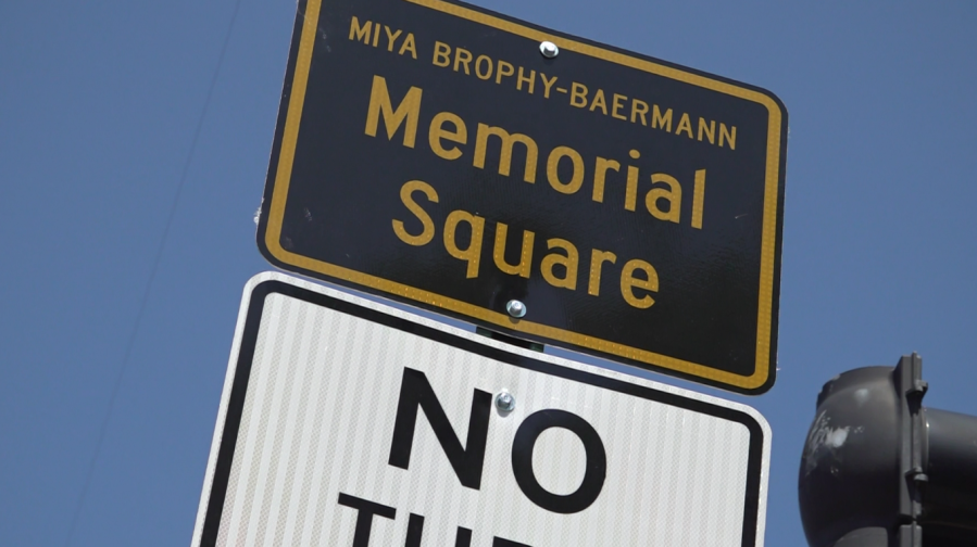 Sign for Miya Brophy-Baermann Memorial Square with a "No Turn" traffic sign below. Clear blue sky in the background.