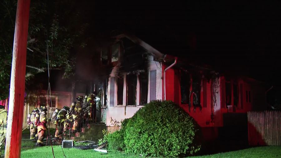 Firefighters respond to a house fire at night, with smoke billowing from the damaged structure.