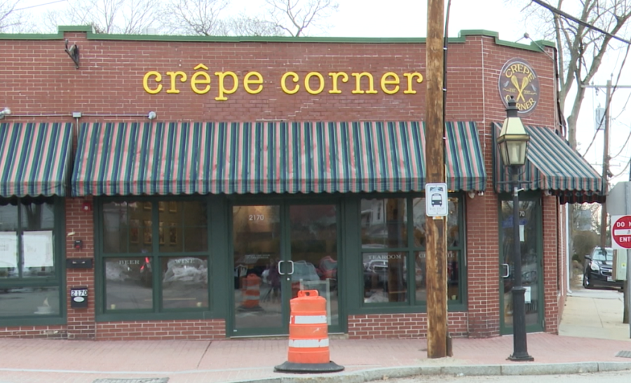 Brick building with "crêpe corner" sign, striped awning, and orange traffic cone in front.