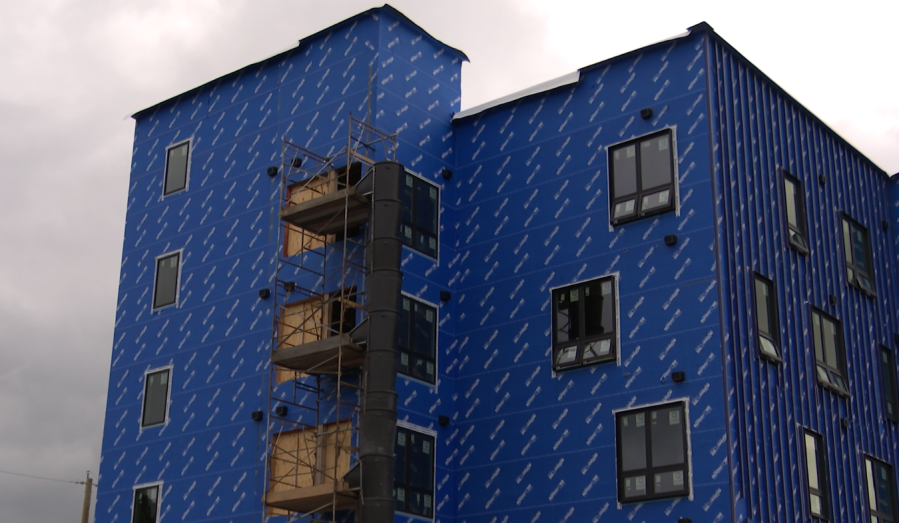 Construction site of a blue-wrapped building with scaffolding and several windows.