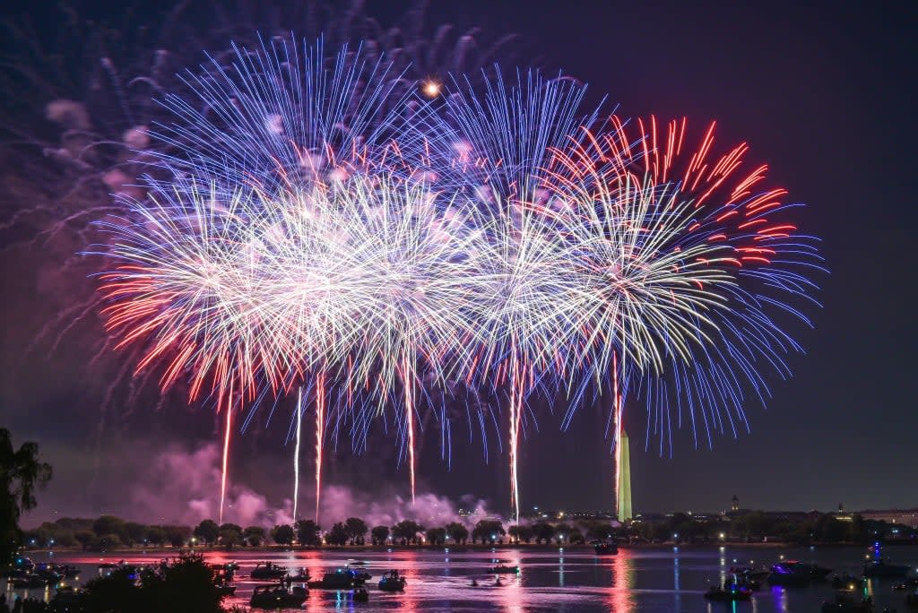 Colorful fireworks illuminate the night sky over a body of water, with boats visible below.