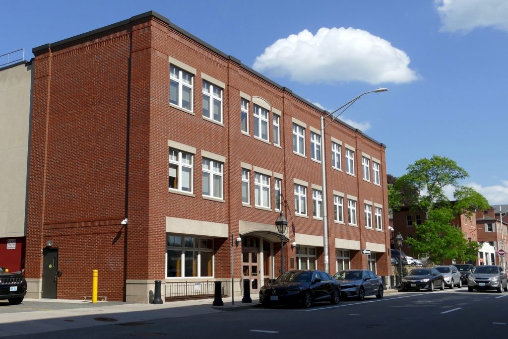 Red brick building with multiple windows, street lamps, and parked cars along the road.