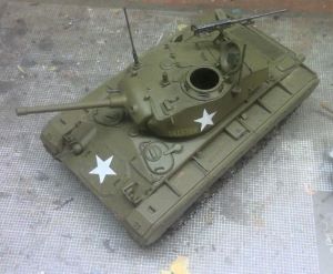 A detailed model of a military tank with white stars, positioned on a textured surface.