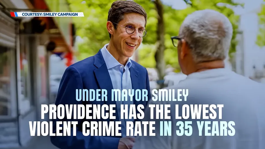 A man in glasses smiles while speaking to another man outdoors, with text highlighting crime rate improvements.