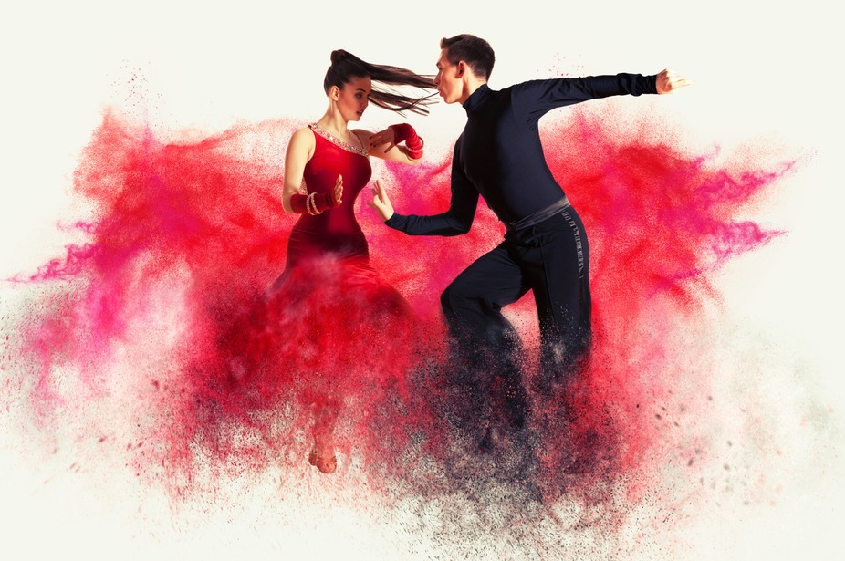 A man and woman dance dynamically, surrounded by vibrant red powder.