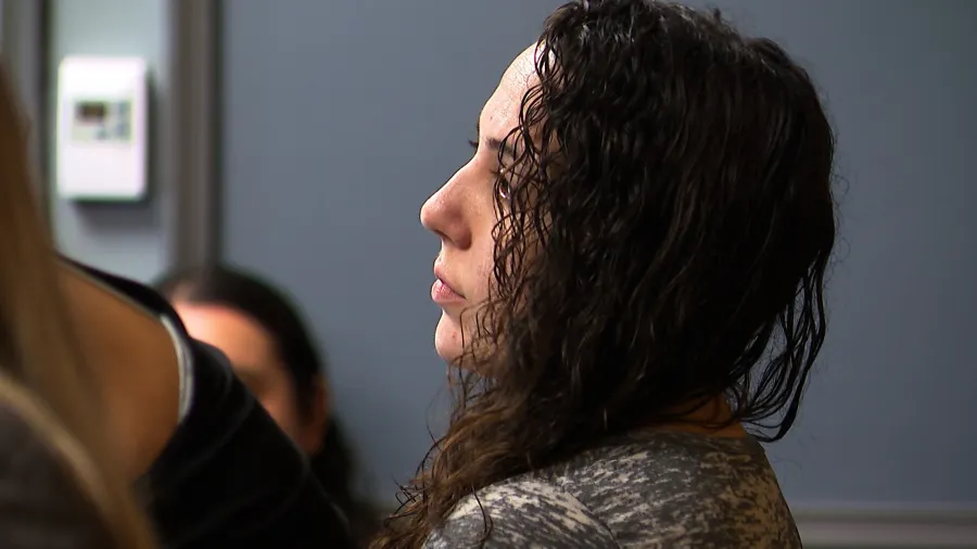 A woman with curly hair sits in profile, looking thoughtfully to the side in a meeting or discussion setting.