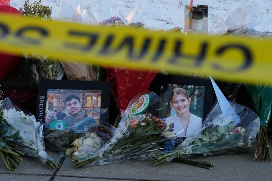 Memorial with flowers and photos of two individuals, marked by police tape.