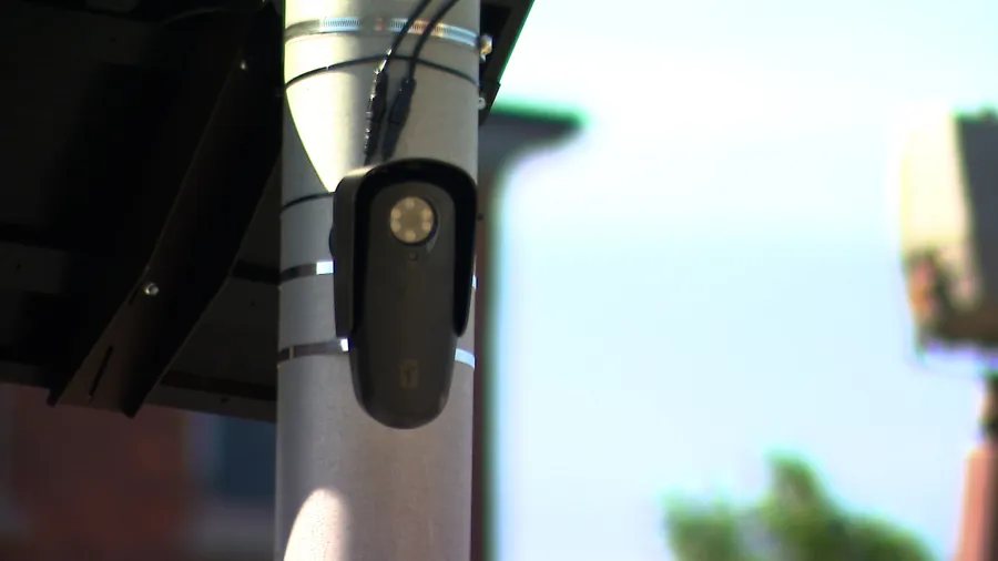 A mounted camera on a pole, connected with wires, against a blurred background.