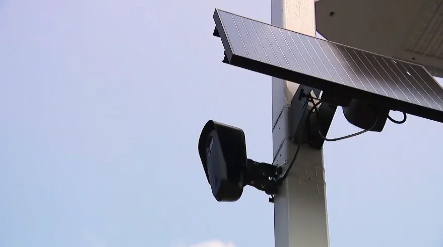 A solar panel powers a Flock camera mounted on a pole, capturing images in the environment.